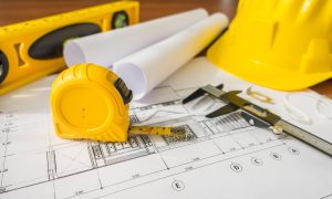 Construction plans with yellow helmet and drawing tools on blueprints